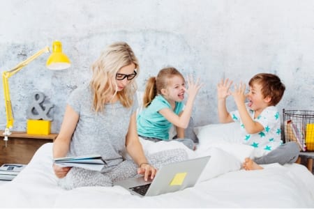 mom working on bed with kids playing behind