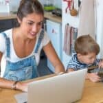 mum working on laptop next to boy playing on tablet