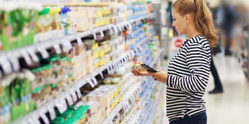 Girl standing in supermarket aisle holding jar of baby food