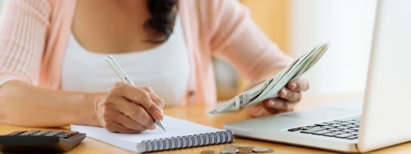 woman sitting at desk with pen and paper in one hand and money in the other