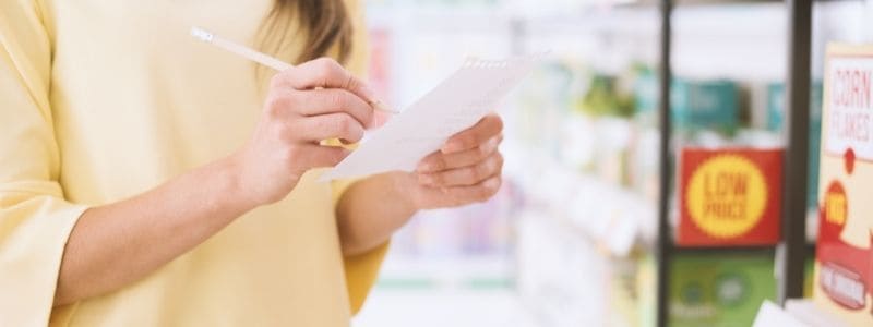 woman marking items off list in grocery store