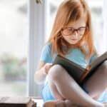Young girl sitting cross-legged reading a book