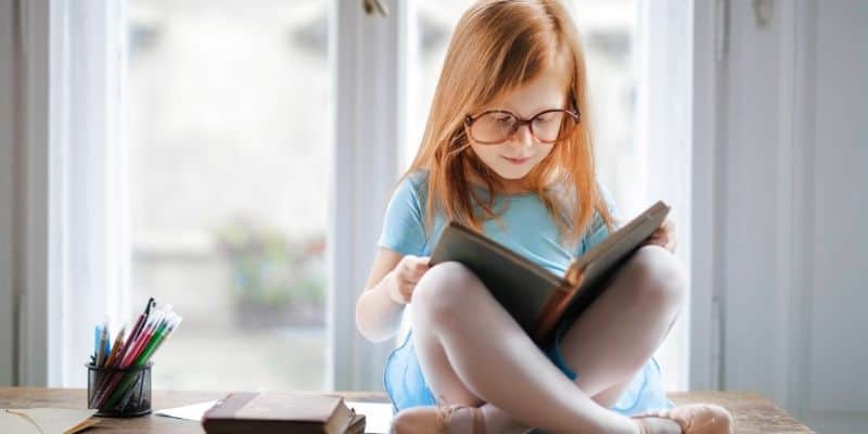 Young girl sitting cross-legged reading a book