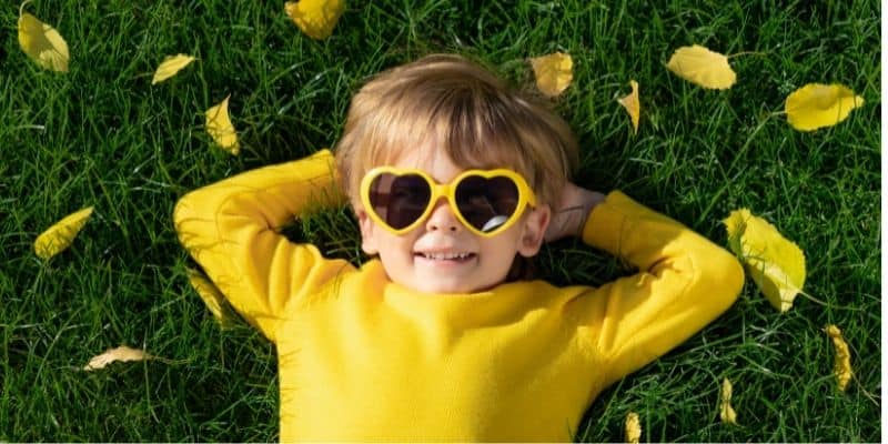 child laying on grass wearing heart shape yellow sunglasses