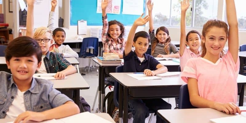pupils sitting at desks with raised hands