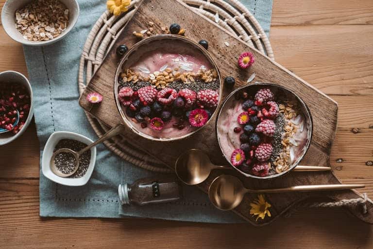 Top view of berry smoothie bowls with granola on a rustic wooden board, perfect vegan breakfast.