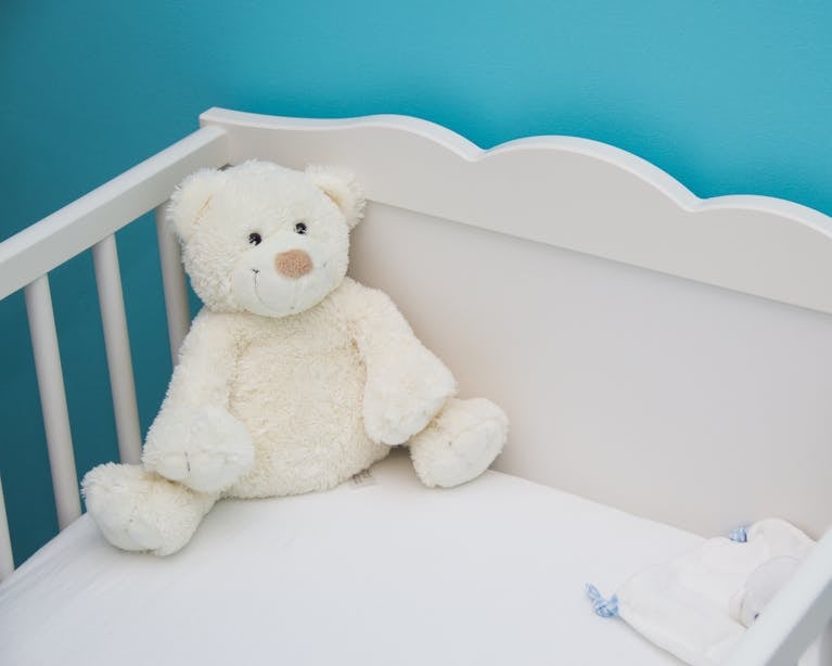 Soft teddy bear in a white crib against a vibrant blue wall, creating a comforting nursery atmosphere.