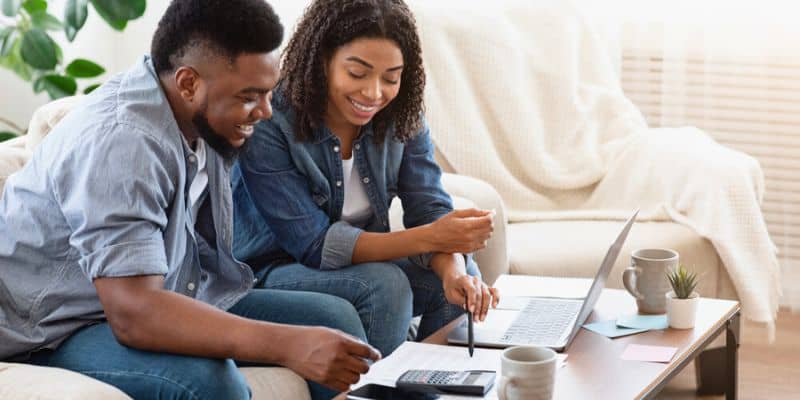 Couple sitting together working out finances on laptop with calculator and coffee