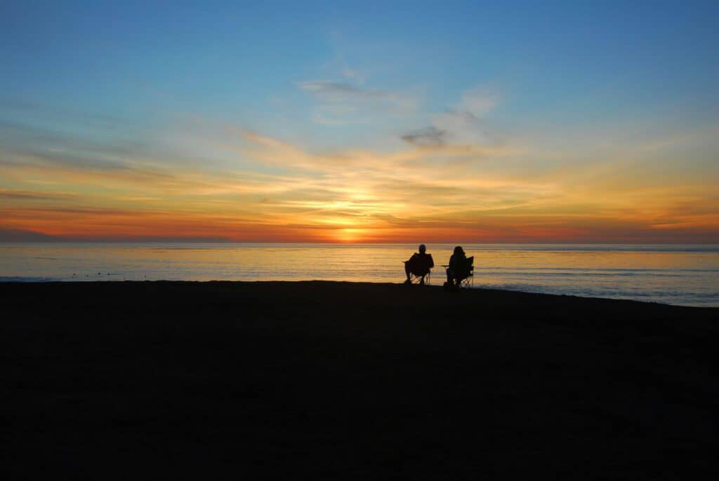 two people sitting in chairs on beach at sunrise
